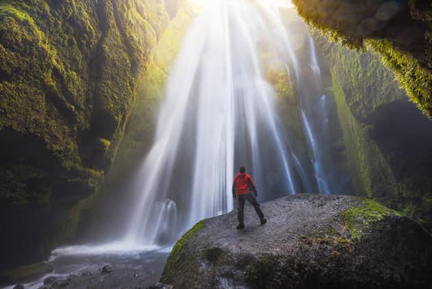 photo of man looking at the gljufrabui waterfall inside a cave in Iceland.