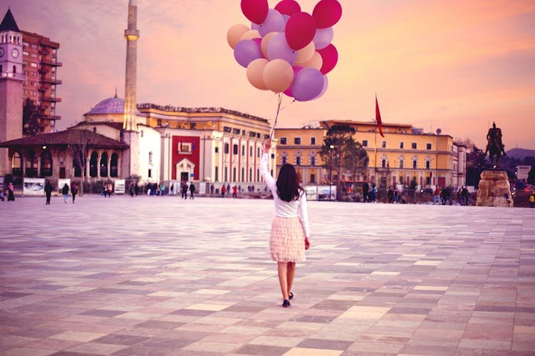 Young woman with a lot of balloons walking in Tirana central square in evening dreamy scenic sunset.