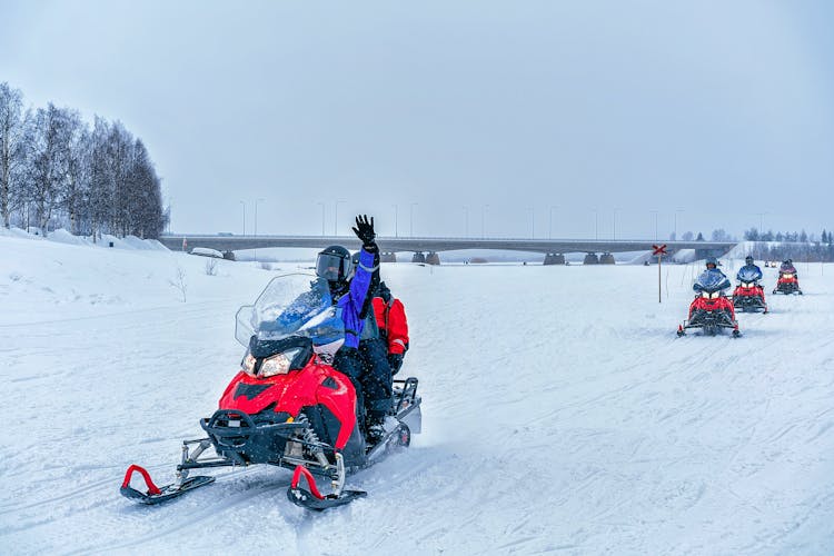 photo of people on snowmobile waving hand on the frozen lake in winter Rovaniemi, Lapland, Finland.