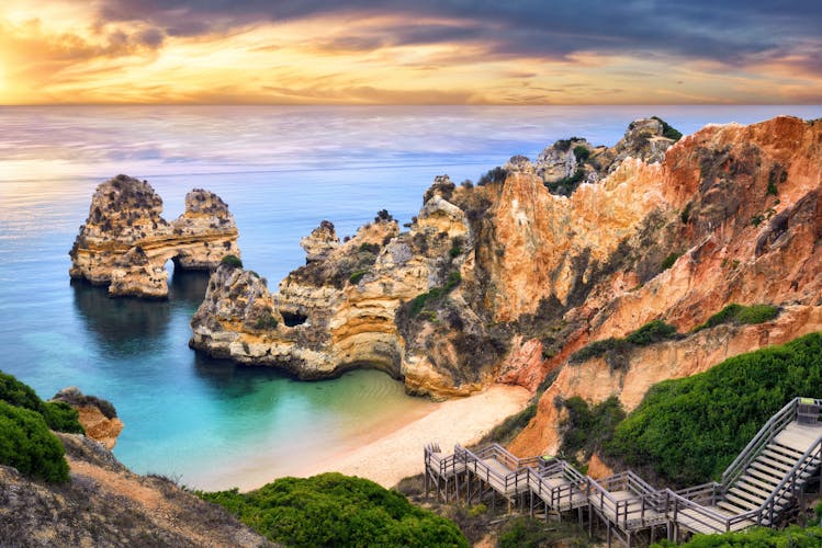 Photo of the beautiful Camilo beach in Lagos, Portugal, with its magnificent cliffs and the blue ocean colorfully lit at sunrise.