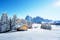 photo of winter landscape with wooden log cabin on meadow Alpe di Siusi on blue sky background on sunrise time. Dolomites, Italy. Snowy hills with orange larch and Sassolungo and Langkofel mountains group.