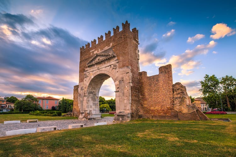 Photo of Arch of Augustus in Rimini. Famous destination in Rimini triumphal arch. Augustus arch on blue sky background in morning.
