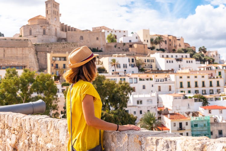 Photo of woman tourist looking at the cathedral of Santa Maria de la Neu from the castle wall of Ibiza.