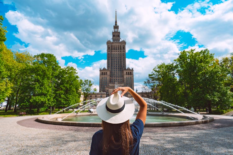 Photo of tourist woman in white sun hat walking in the park near Palace of Culture and Science in Warsaw.