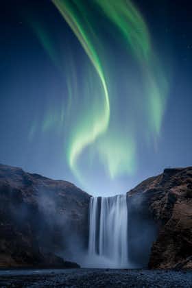 photo of a beautiful auora borealis aka northern lights over skogafoss waterfall in Iceland.