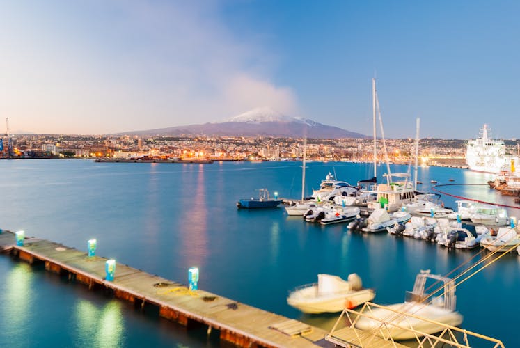 Skyline of Catania and its harbor with snowy volcano Etna in background.