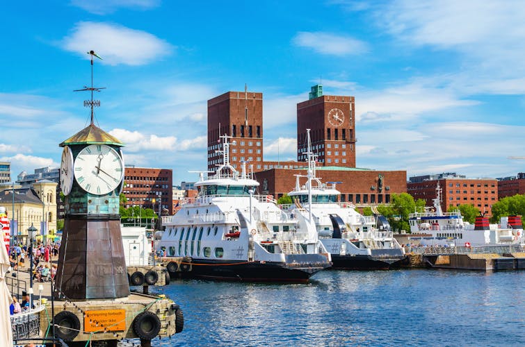Photo of the Clock on Aker Brygge Dock with the background of the famous Oslo City Hall and the harbor, Oslo Fjord, Norway.