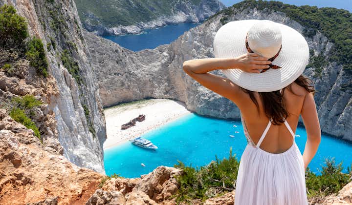 Photo of woman stands on a cliff and enjoys the breathtaking view to the famous shipwreck beach, Navagio, on Zakynthos island, Greece.