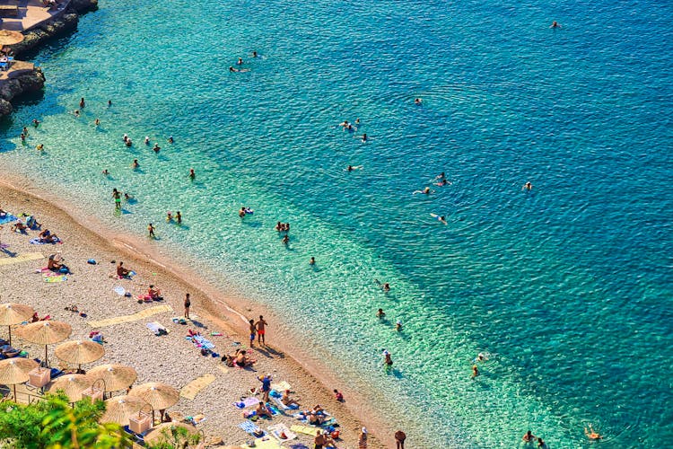 Photo of people on the Nafplio beautiful beach with clear water and blue sky, in the Peloponnese peninsula in Greece.