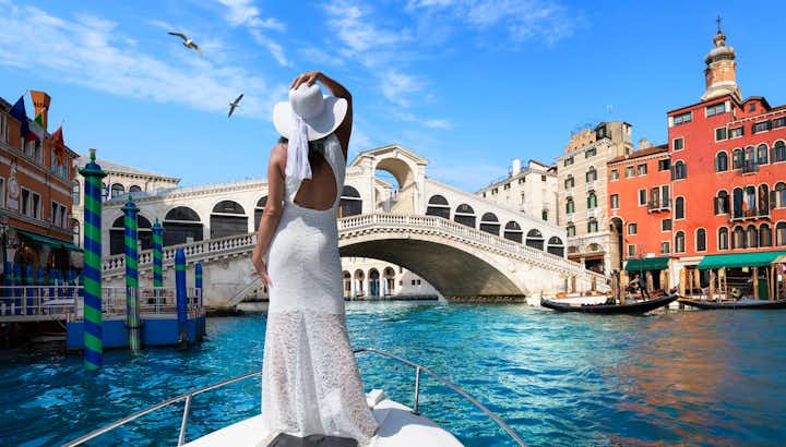 photo of beautiful woman with a white dress is standing on a boat in front of the famous rialto bridge in Venice.