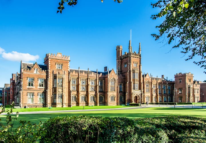 Photo of the Queen's University of Belfast with a grass lawn, tree branches and a hedge in sunset light.