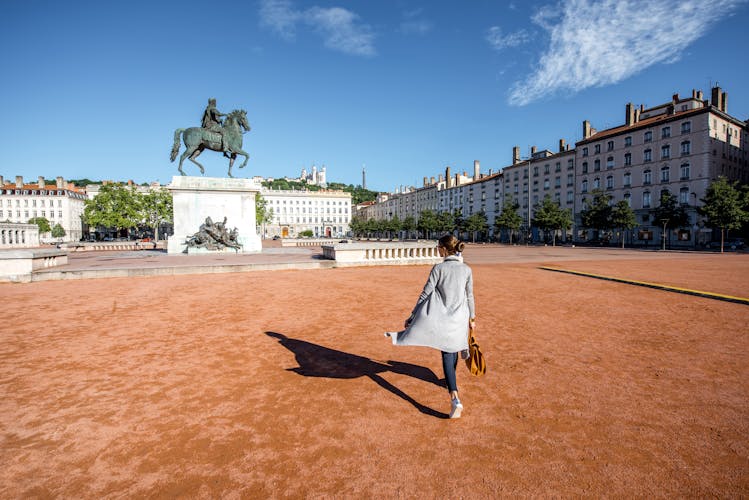 Photo of woman walking on the famous Bellecour square with Louis king statue traveling in Lyon city in France.