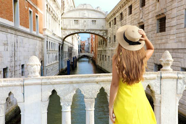 photo of Travel in Venice. Back view of pretty girl in yellow dress holding hat looking at Bridge of Sighs in Venice, Italy. Beautiful young woman visiting Europe.