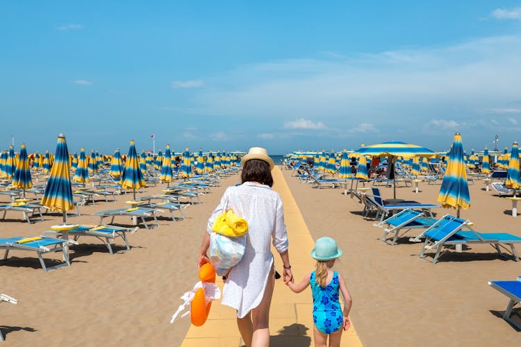 Photo of Woman and child outdoors. Mother and daughter going to rest on beach. Rimini, Italy.