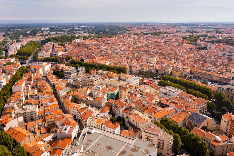 Photo of bird's eye view of Perpignan, France. Red rooftops of residential buildings visible from above.