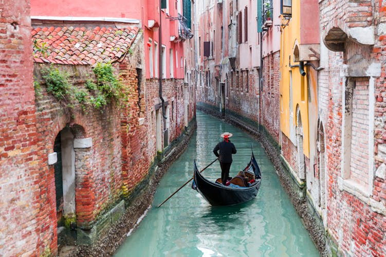 Venetian gondolier punting gondola through green canal waters of Venice, Italy.