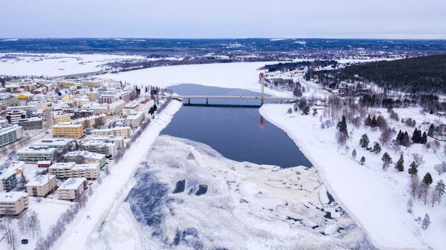 Photo of beautiful winter landscape with buildings and a bridge over Ounasjoki River in Rovaniemi.