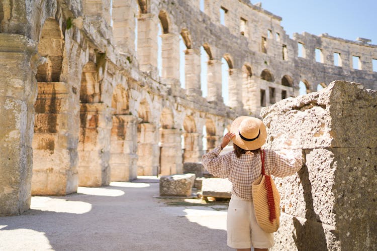 Photo of woman in hat stands and looking on Coliseum in Pula.