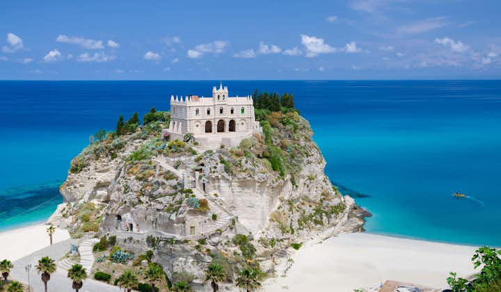 Monastery Sanctuary church of Santa Maria dell Isola on top of rock Tyrrhenian Sea and green palm trees, blue sky white clouds in summer clear day, Tropea town.