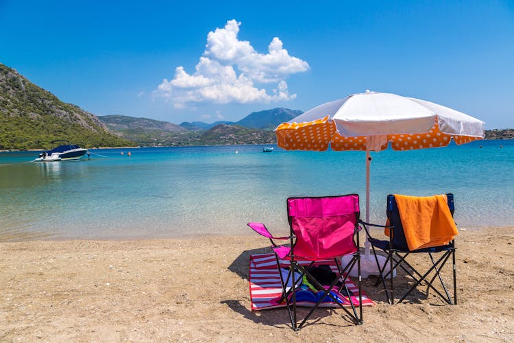 Photo of umbrella and sundecks on beautiful sandy beach near Loutraki in a summer day with blue sky, Greece.