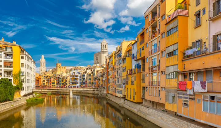 Colorful yellow and orange houses and bridge Pont de Sant Agusti reflected in water river Onyar, in Girona, Catalonia, Spain. Church of Sant Feliu and Saint Mary Cathedral at background