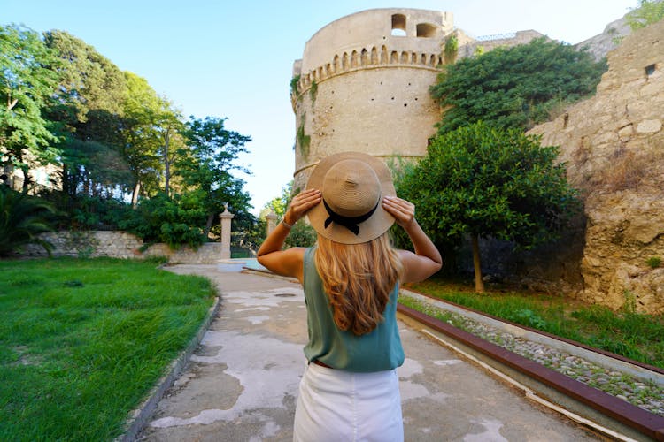 Photo of Tourism in Calabria. Back view of beautiful woman in Crotone with Charles V Aragon Castle in Crotone, Calabria, Italy.