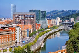 Photo of aerial view of Bilbao, Spain city downtown with a Nevion River, Zubizuri Bridge and promenade. Mountain at the background, with clear blue sky.