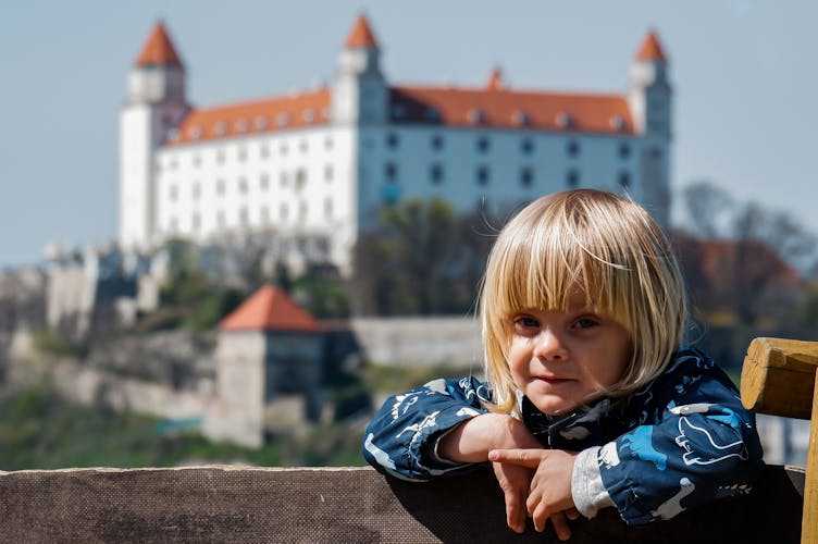 Blond boy with long hair in front of the castle.