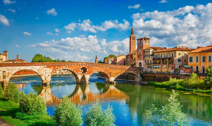 Panoramic view to Bridge Ponte Pietra in Verona on Adige river. Veneto region. Italy. Sunny summer day panorama and blue dramatic sky with clouds. Ancient european italian terracotta color houses