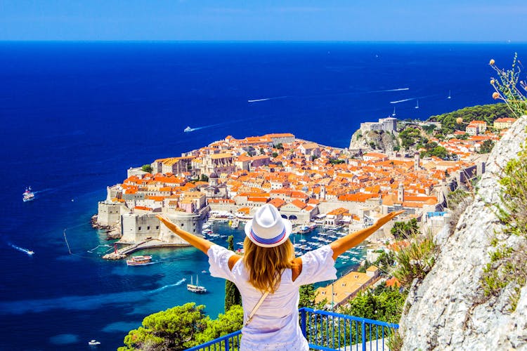 Photo of happy woman enjoys beautiful landscape view of old town (medieval Ragusa) and Dalmatian Coast of Adriatic Sea in Dubrovnik, Croatia.