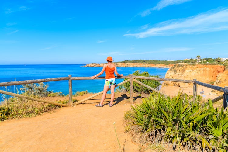 Photo of tourist standing on cliff and looking at beautiful sea coast, Portimao town, Portugal
