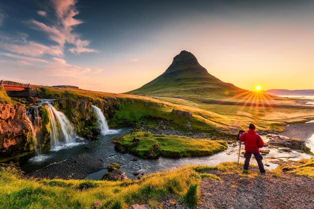  photo of panorama landscape of sunrise over volcanic kirkjufell mountain with kirkjufellsfoss waterfall and photographer man standing in summer at Snaefellsnes peninsula, Iceland.