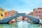 Stone bridge Ponte di Vigo across Vena water canal with colorful boats and old buildings in historical centre of Chioggia town, blue sky background in summer day, Veneto Region, Northern Italy