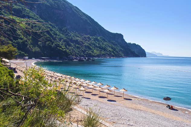 Photo of Jaz beach near Budva on the background of rocky hills covered with trees, calm blue sea. Blue cloudless morning sky, rows of straw umbrellas, Montenegro.