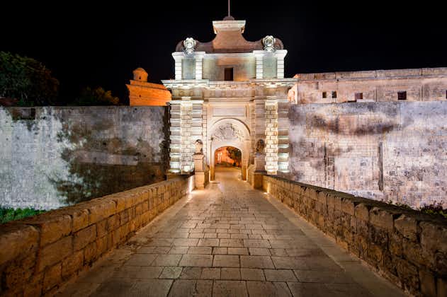 Photo of entrance bridge and gate to Mdina at night, a fortified medieval city in the Northern Region of Malta.