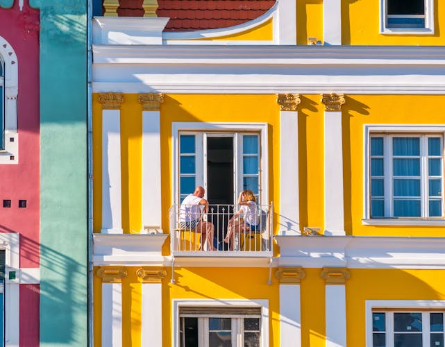 Man and woman sitting on a small balcony of an old colored building right in the center of Timisoara.