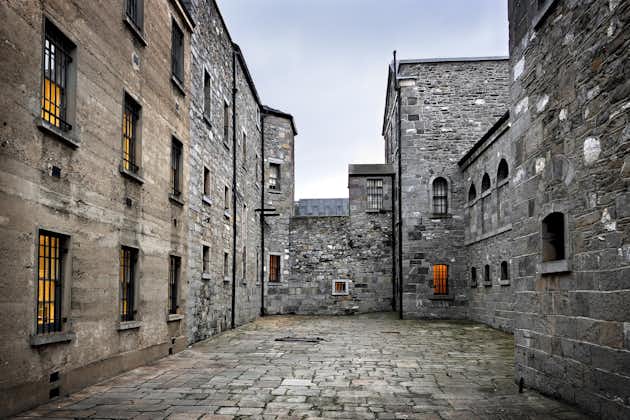 photo of Paved courtyard of ancient prison, surrounded by massive stone walls with lit windows. Kilmainham Gaol, Dublin, Ireland.