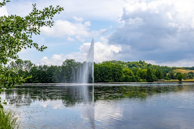 Echternach lake with a waterjet and breeze from a fountain, hills and green leafy trees on misty background, reflection on water surface, sunny spring day with abundant clouds in Luxembourg.