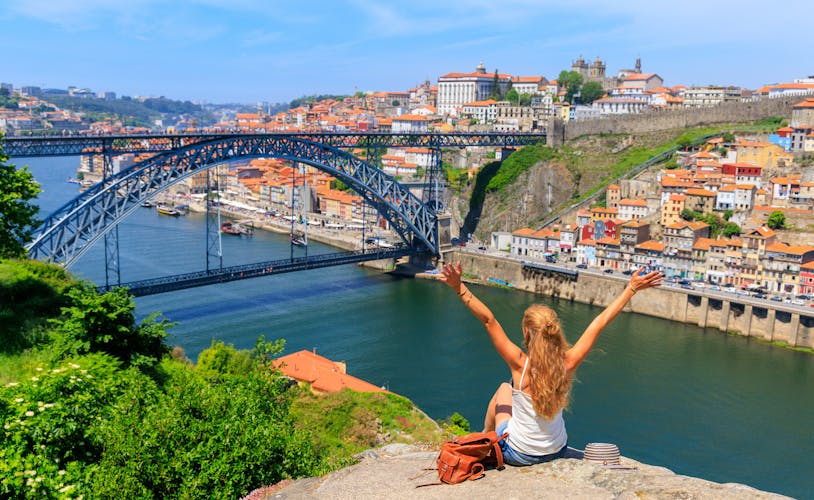 Photo of Woman touristwith arms raised enjoying beautiful panoramic view of famous iron bridge and old town- tour in Porto.