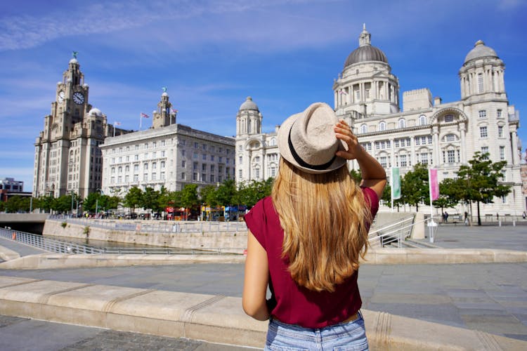 Photo of tourist woman visiting Pier Head with "The Three Graces" in the city centre of Liverpool, England.