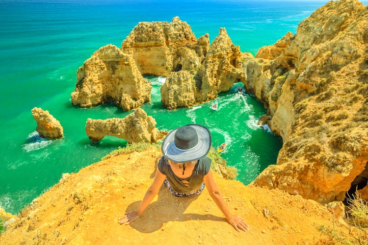 Photo of  tourist sitting on promontory of Ponta da Piedade, woman looking amazing views of iconic cliffs of turquoise sea of Lagos.