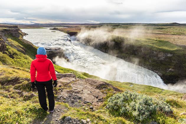 photo of Iceland travel gullfoss waterfall tourist woman looking over icelandic falls, famous attraction on the golden circle. Nature lansdcape in summer, spring or autumn.