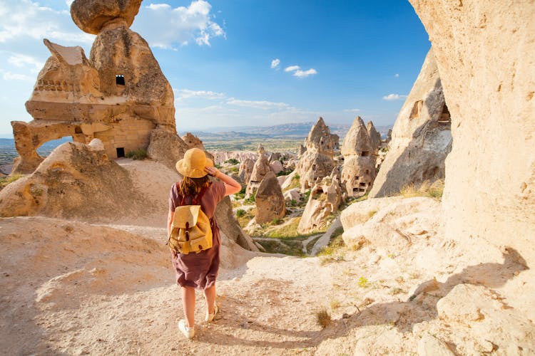 Photo of woman exploring valley with rock formations and fairy chimneys near Uchisar castle in Cappadocia Turkey.