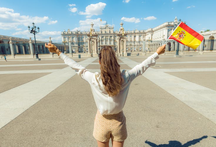 Photo of tourist woman with Spain flag rejoicing against Royal Palace in Madrid.