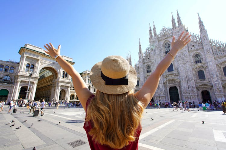 Photo of tourist woman with arms raised in Milan Cathedral Square, Italy.