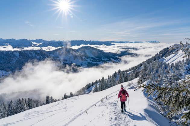 photo of nice senior woman snowshoeing on the Nagelfluh chain above a sea of fog over Bregenz Wald mountains, Hochgrat, Steibis, Bavarian alps, Germany.