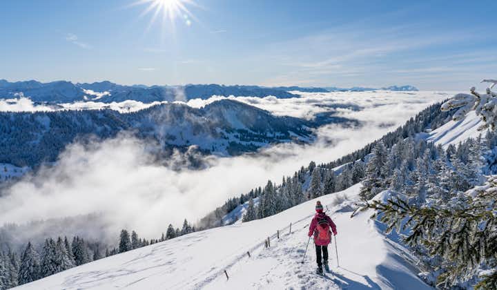 photo of nice senior woman snowshoeing on the Nagelfluh chain above a sea of fog over Bregenz Wald mountains, Hochgrat, Steibis, Bavarian alps, Germany.