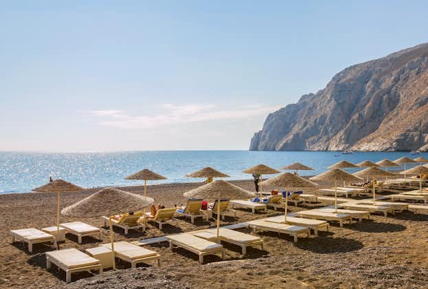 Photo of beach chairs and umbrellas on Kamari beach on volcanic island Santorini in the morning, Greece.