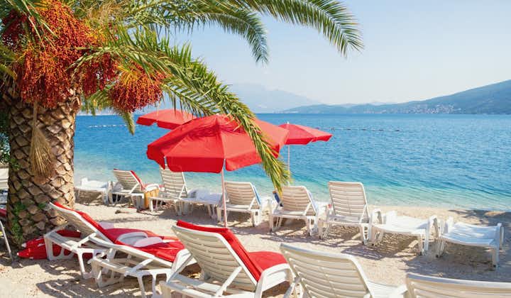 Photo of sunny Mediterranean landscape with red beach umbrellas. Montenegro, Adriatic Sea, Bay of Kotor, Herceg Novi.