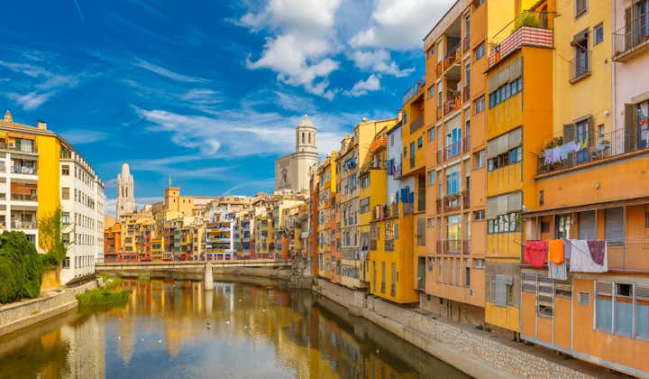 Colorful yellow and orange houses and bridge Pont de Sant Agusti reflected in water river Onyar, in Girona, Catalonia, Spain. Church of Sant Feliu and Saint Mary Cathedral at background
